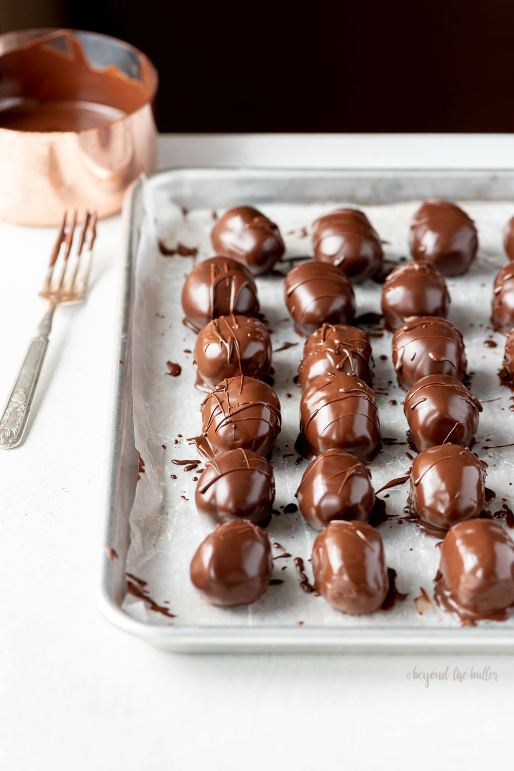 Angled photo of chocolate covered peanut butter eggs on a baking sheet | Image and Copyright Policy: © Beyond the Butter, LLC