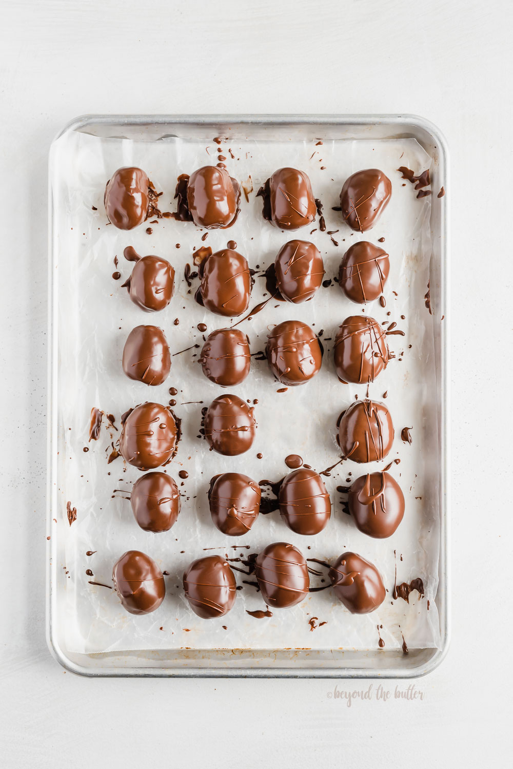 Overhead photo of chocolate covered peanut butter eggs on a baking sheet with one removed | Image and Copyright Policy: © Beyond the Butter, LLC