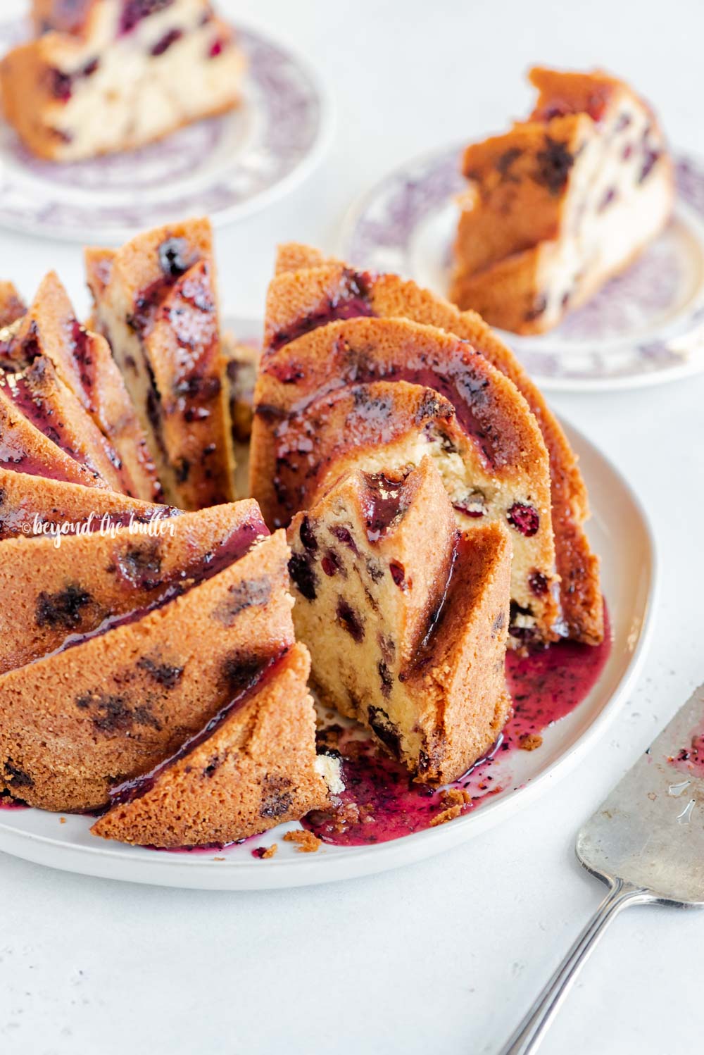 Angled image of sliced blueberry bundt cake with blueberry glaze drizzled over the top | All Images © Beyond the Butter, LLC