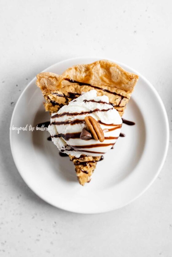 Overhead image of one slice of chocolate chip pie with a scoop of vanilla ice cream on top drizzled with chocolate syrup | All Images © Beyond the Butter™