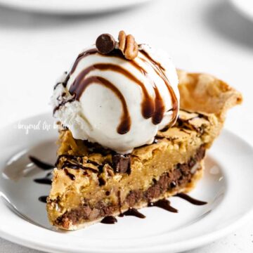 Angled closeup image of Chocolate Chip Pie with a scoop of vanilla ice cream on top that's drizzled with chocolate syrup | All Images © Beyond the Butter™