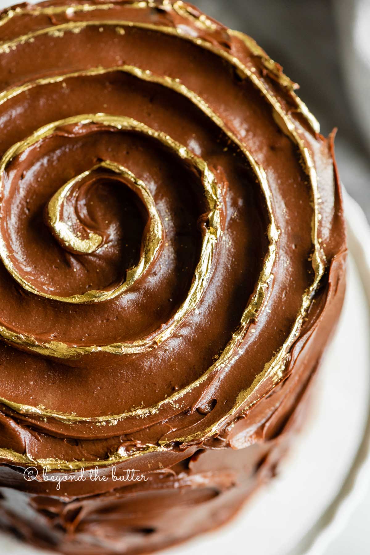 Angled closeup image of chocolate zucchini cake with gold decorative swirl on top | All Images © Beyond the Butter™