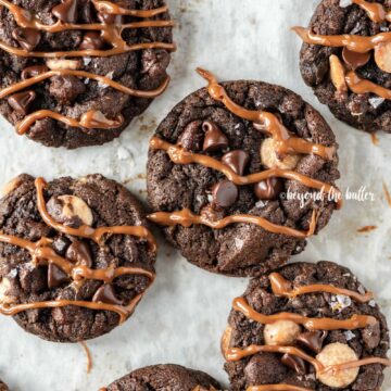 Overhead image of just baked double chocolate salted caramel cookies on a baking sheet with caramel drizzled over the top of each cookie | All Images © Beyond the Butter™