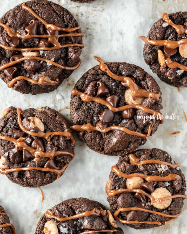 Overhead image of just baked double chocolate salted caramel cookies on a baking sheet with caramel drizzled over the top of each cookie.