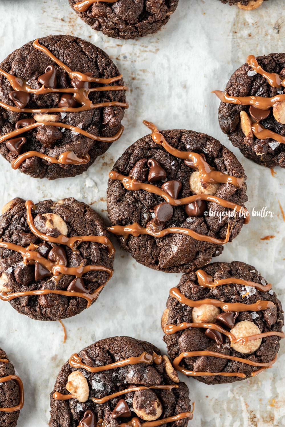 Overhead image of just baked double chocolate salted caramel cookies on a baking sheet with caramel drizzled over the top of each cookie | All Images © Beyond the Butter™