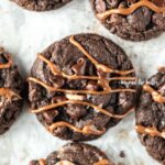 Overhead image of just baked double chocolate salted caramel cookies on a baking sheet with caramel drizzled over the top of each cookie.