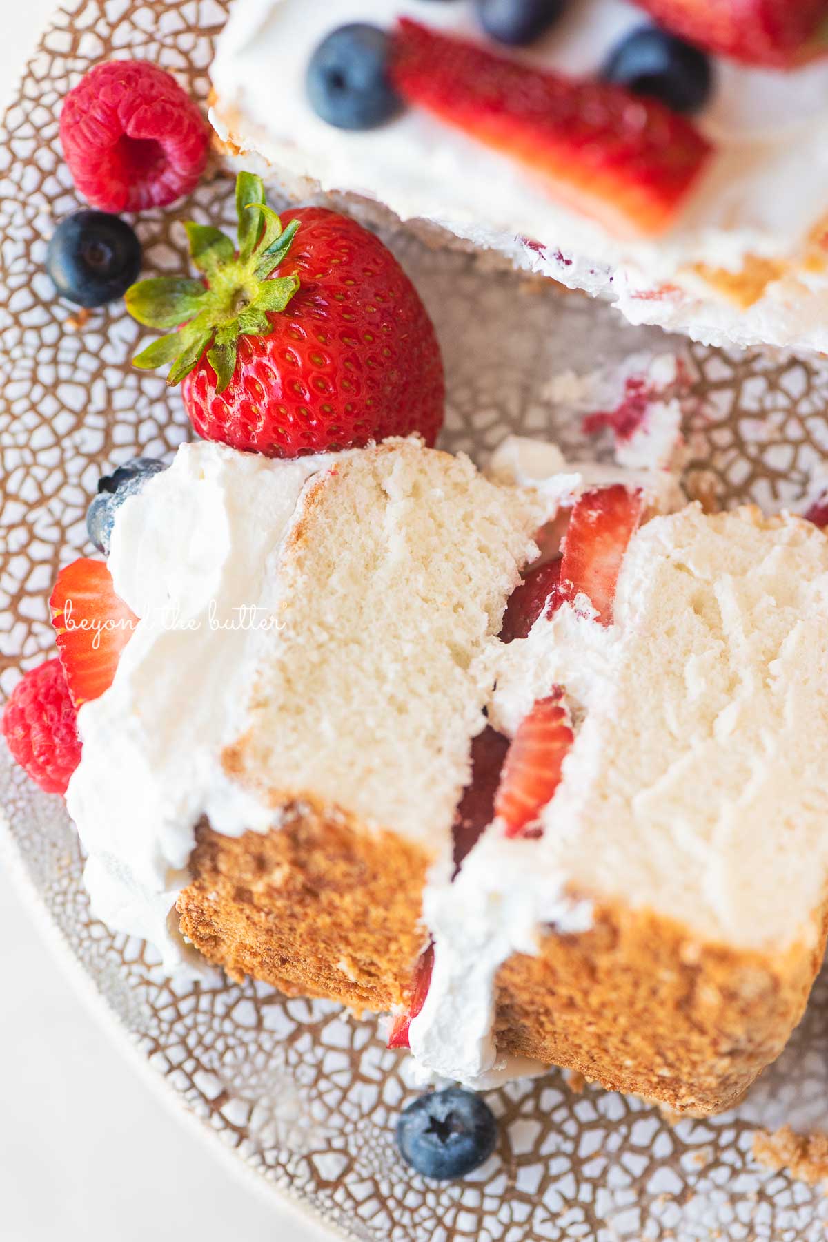 Close up image of angel food cake with one slice on its side on a ceramic cake stand | © Beyond the Butter®
