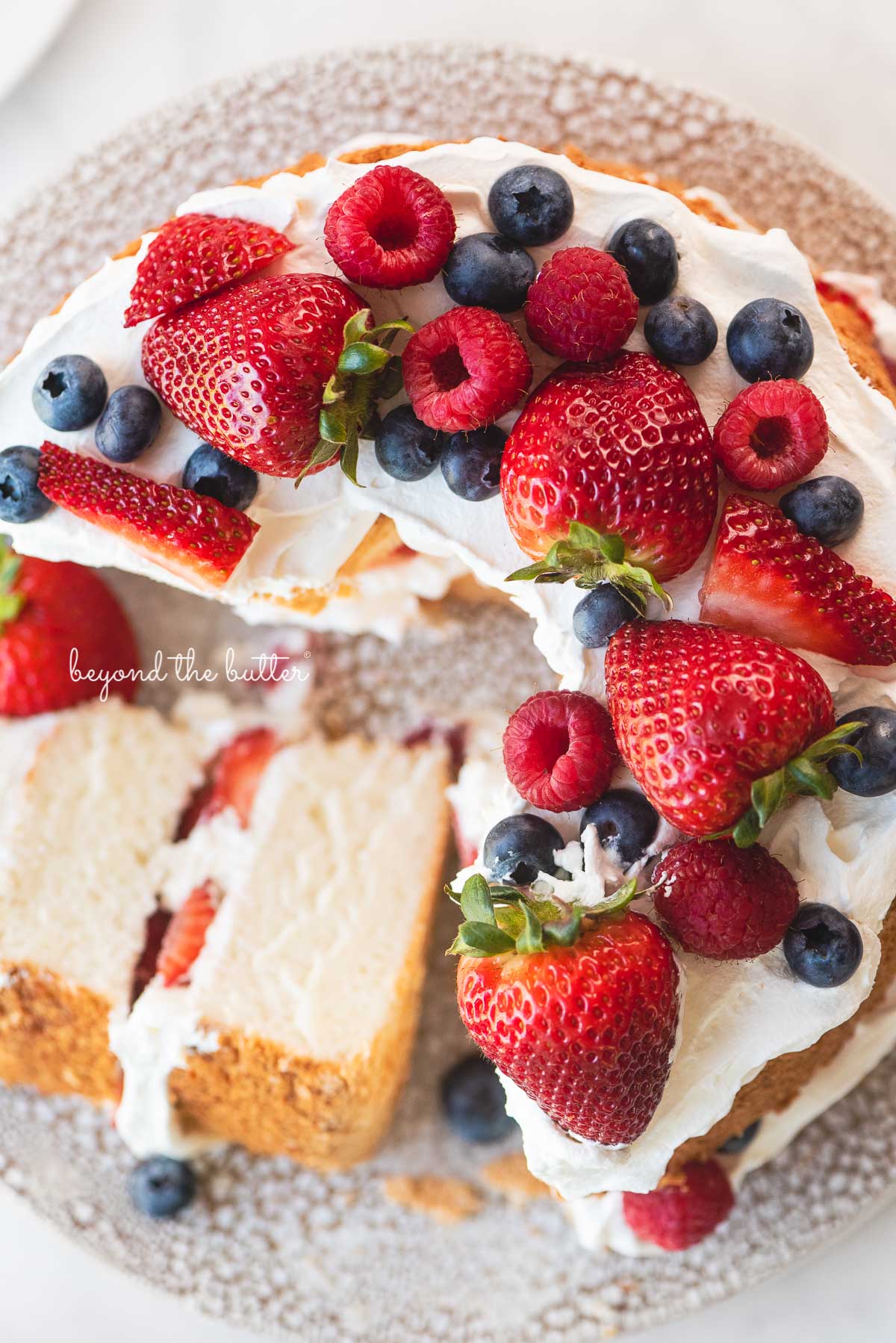 Angel food cake with one slice on its side on a ceramic cake stand | © Beyond the Butter®