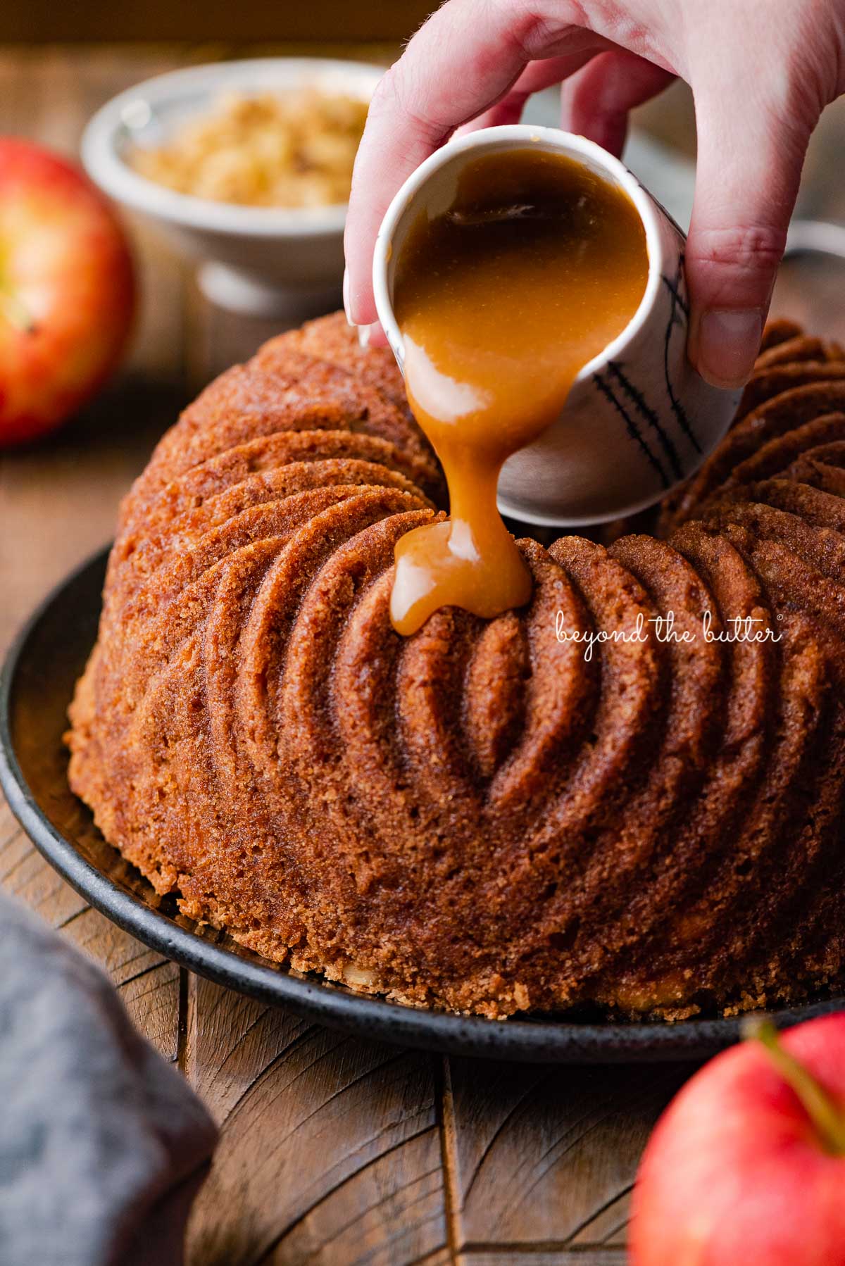 Pouring brown sugar glaze over top of warm apple bundt cake | © Beyond the Butter®