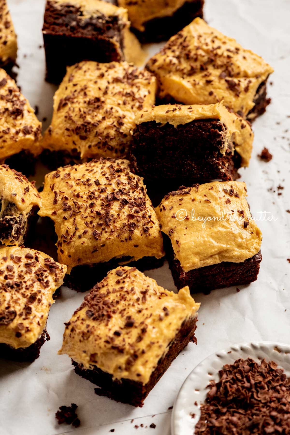 pumpkin frosted brownies randomly placed on parchment paper with a side bowl of chocolate shavings | All Images © Beyond the Butter™