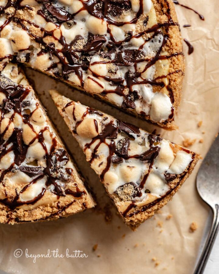 Overhead image of s'mores cheesecake with slice cut out on parchment paper.