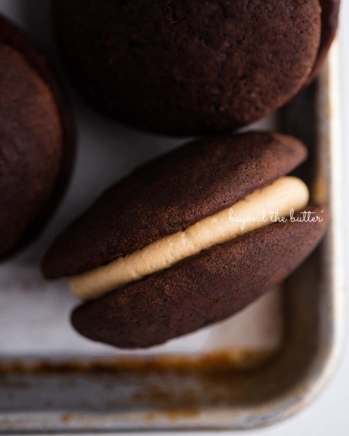 Closeup overhead image of chocolate peanut butter whoopie pies on a parchment lined baking pan.