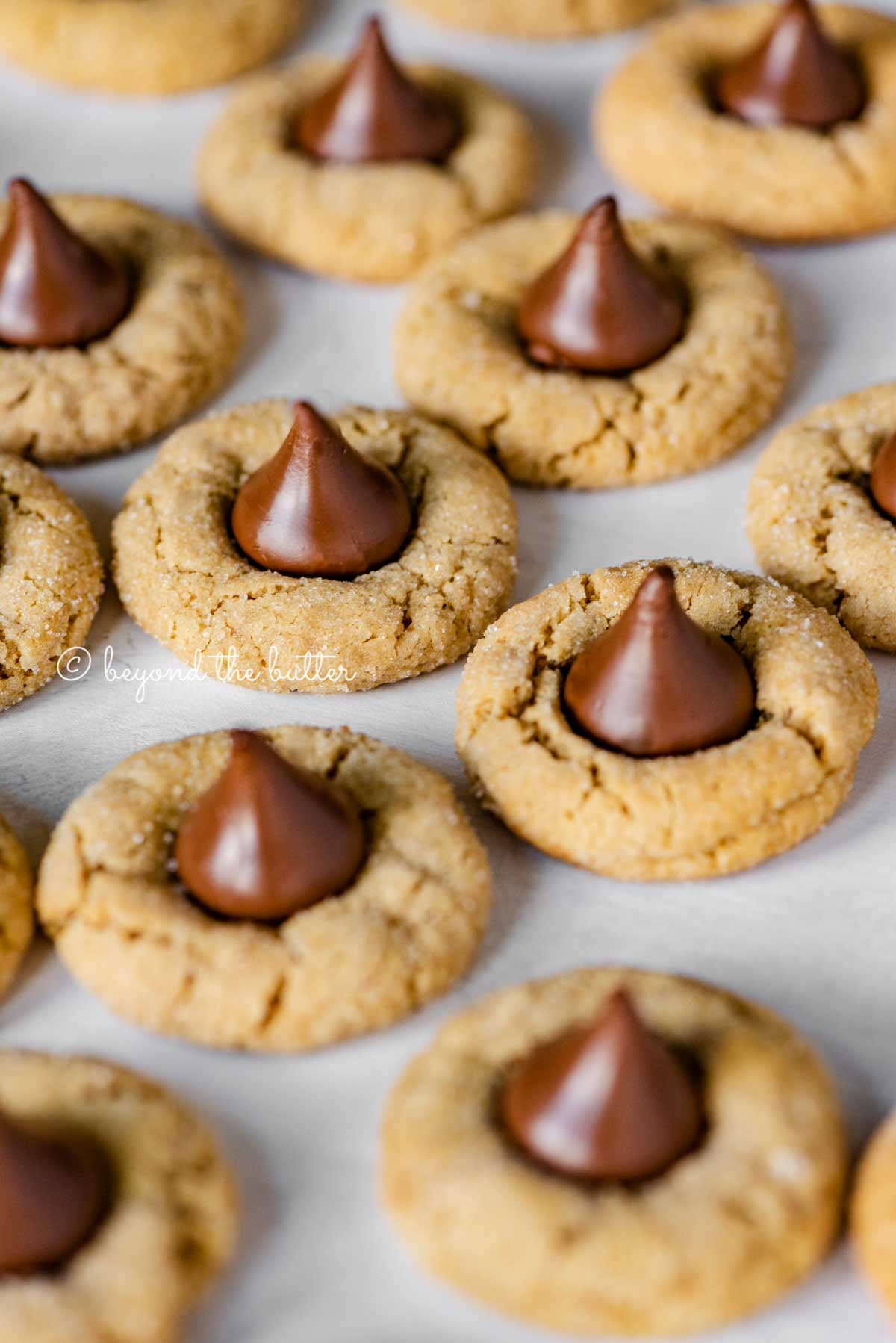 Angled image of peanut butter blossoms on parchment paper lined baking sheet | All Images © Beyond the Butter™
