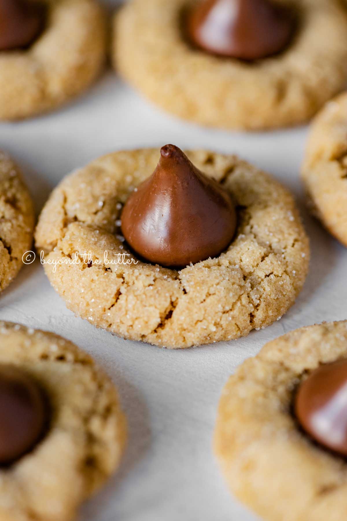 Angled closeup image of peanut butter blossoms on parchment paper lined baking sheet | All Images © Beyond the Butter™