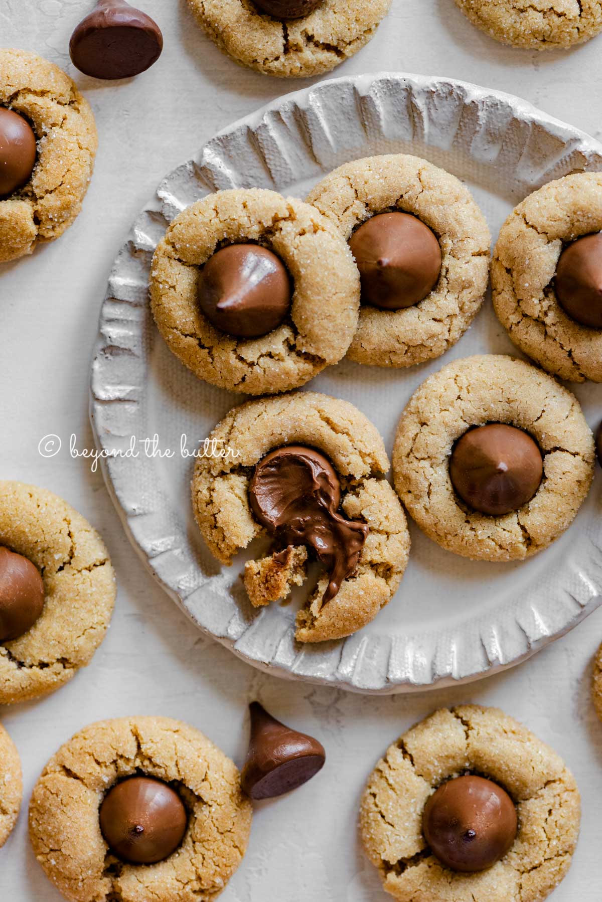 Small dessert plate full of classic peanut butter blossoms with one melted and split apart | All Images © Beyond the Butter™