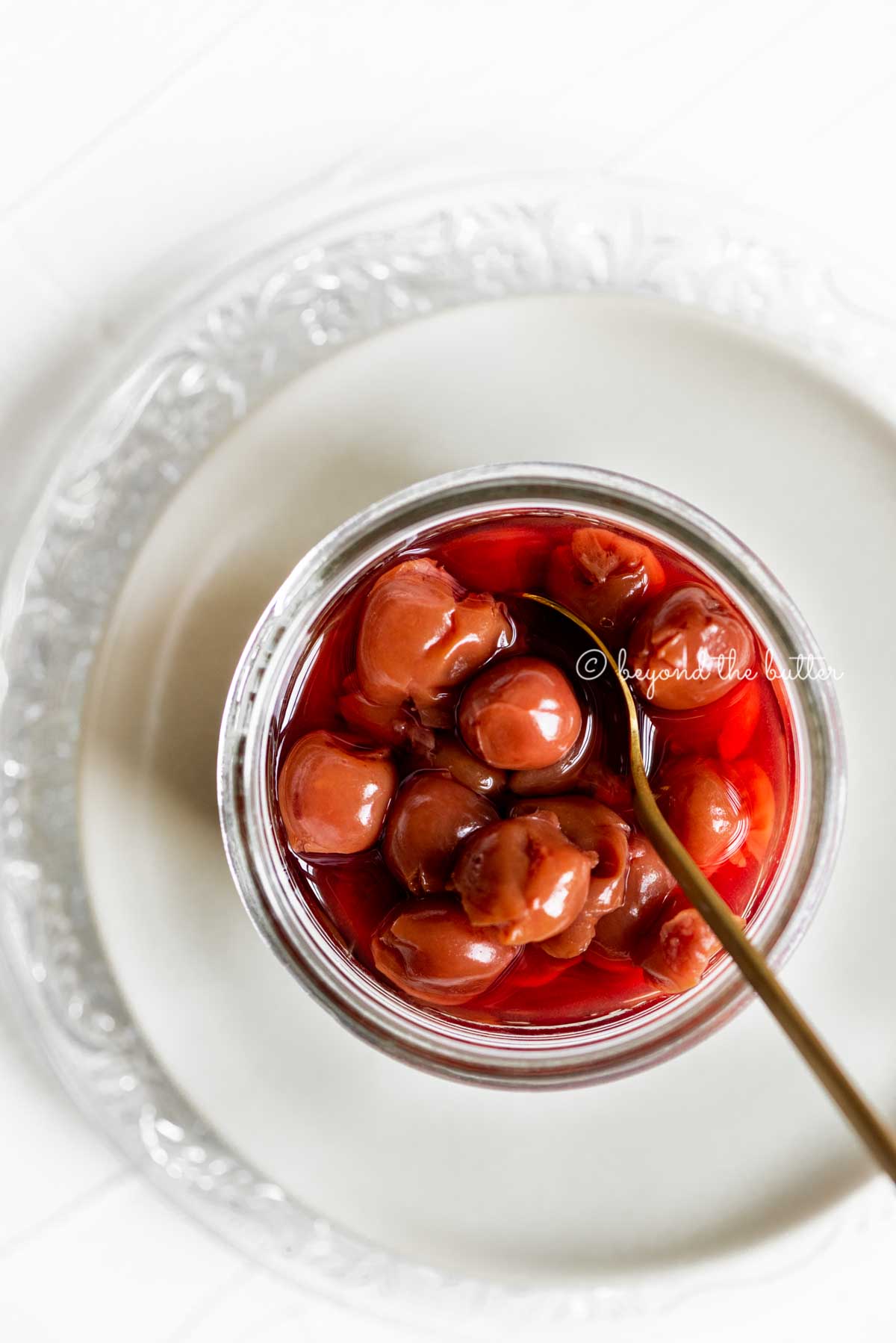 Small glass jar of cherries with a spoon on top of 2 plates | All Images © Beyond the Butter™