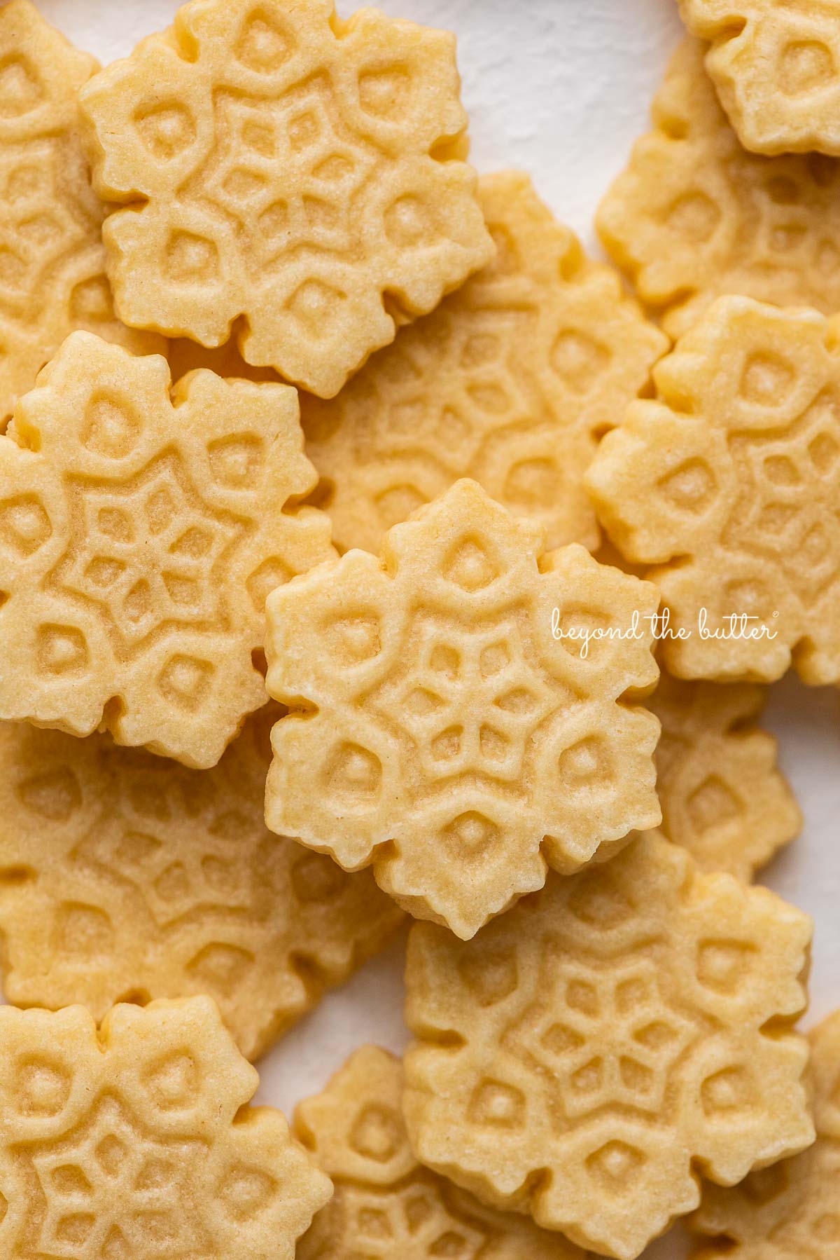 Randomly placed snowflake shaped homemade butter cookies on a white background | © Beyond the Butter®