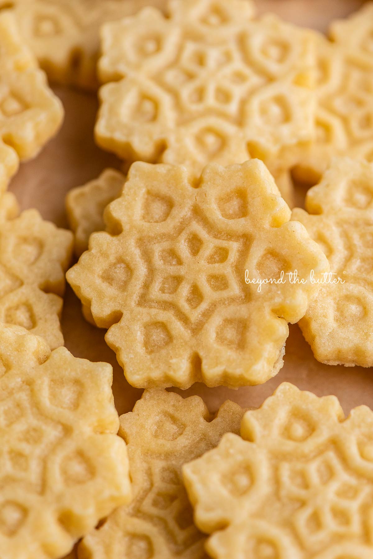 Randomly placed snowflake shaped homemade butter cookies on natural parchment paper background | © Beyond the Butter®