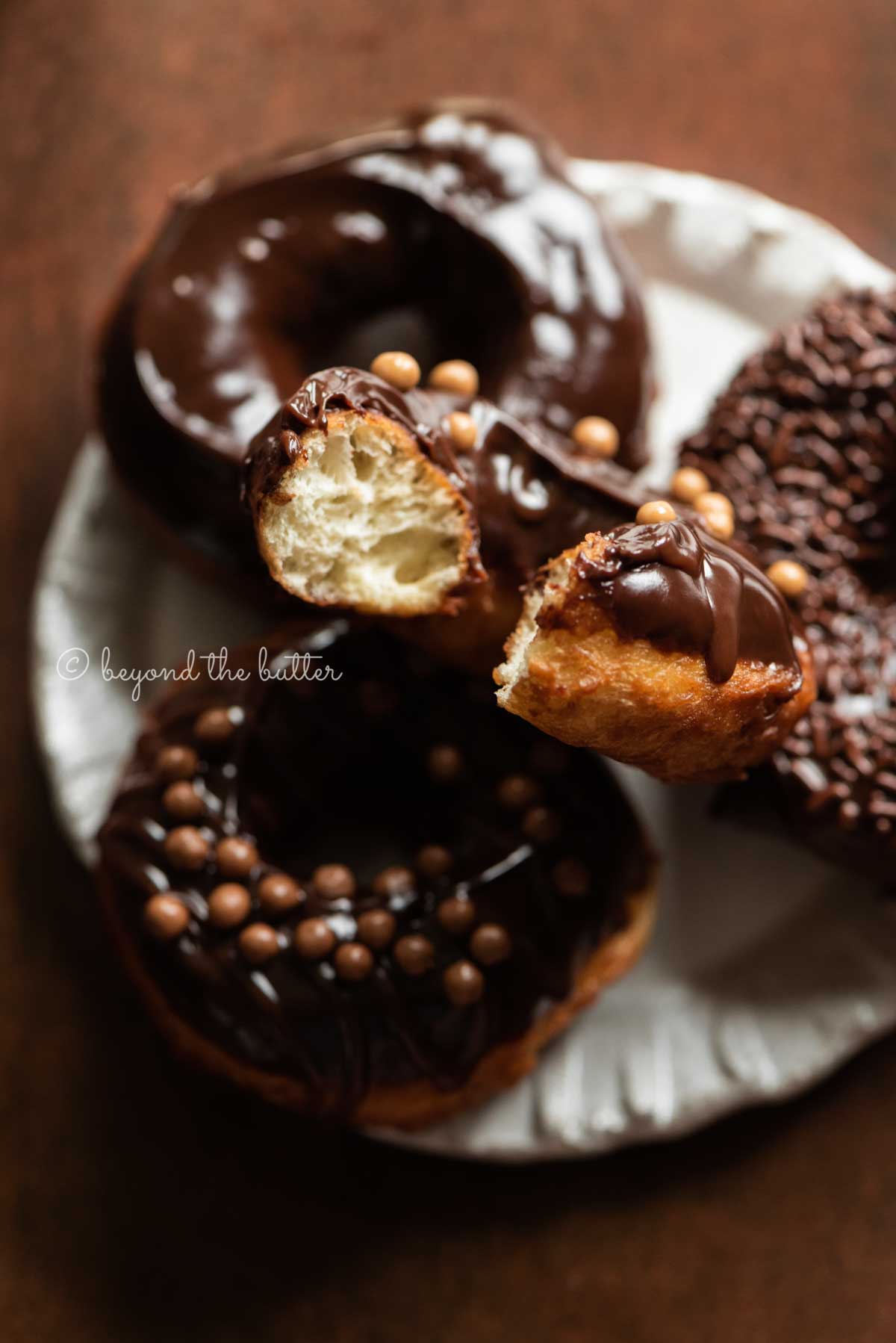 Chocolate glazed donuts stacked on a dessert plate with bite taken out of the top donut | All Images © Beyond the Butter™