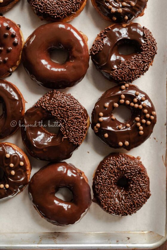 Chocolate glazed decorated donuts on a parchment paper lined baking sheet | All Images © Beyond the Butter™