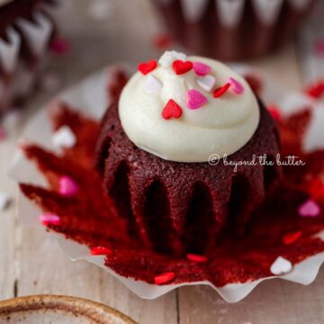 Opened red velvet cupcake with cream cheese frosting topped with heart sprinkles on a light wood background | All images © Beyond the Butter®