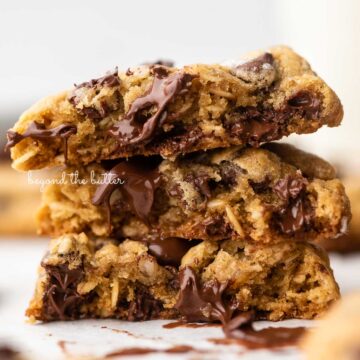 Stack of 3 oatmeal chocolate chip salted caramel cookies on a parchment paper lined baking sheet | © Beyond the Butter®
