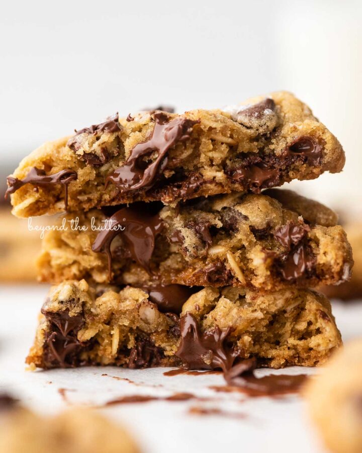 Stack of 3 oatmeal chocolate chip salted caramel cookies on a parchment paper lined baking sheet.