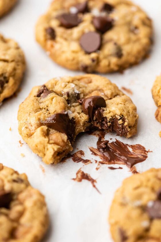 Half eaten oatmeal chocolate chip salted caramel cookie on a white parchment paper background | © Beyond the Butter®