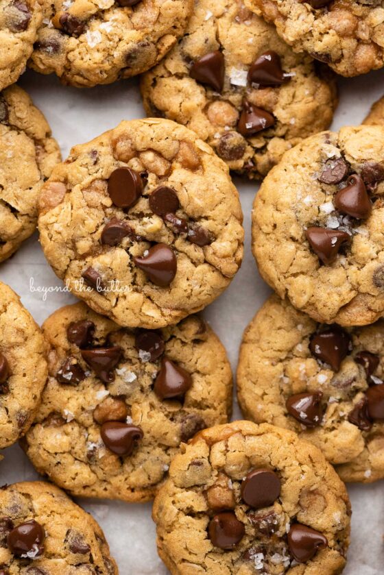 Oatmeal chocolate chip salted caramel cookies topped with flaky sea salt on a parchment paper lined baking sheet | © Beyond the Butter®