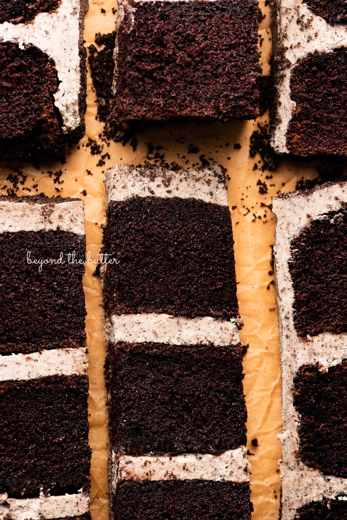 Slices of chocolate cake with oreo buttercream frosting on natural parchment paper.