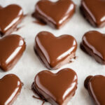 Angled image of chocolate peanut butter hearts that have been dipped in chocolate and placed on wax paper lined cookie sheet.