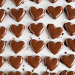 Overhead image of chocolate peanut butter hearts that have been dipped in chocolate and placed on wax paper lined cookie sheet.