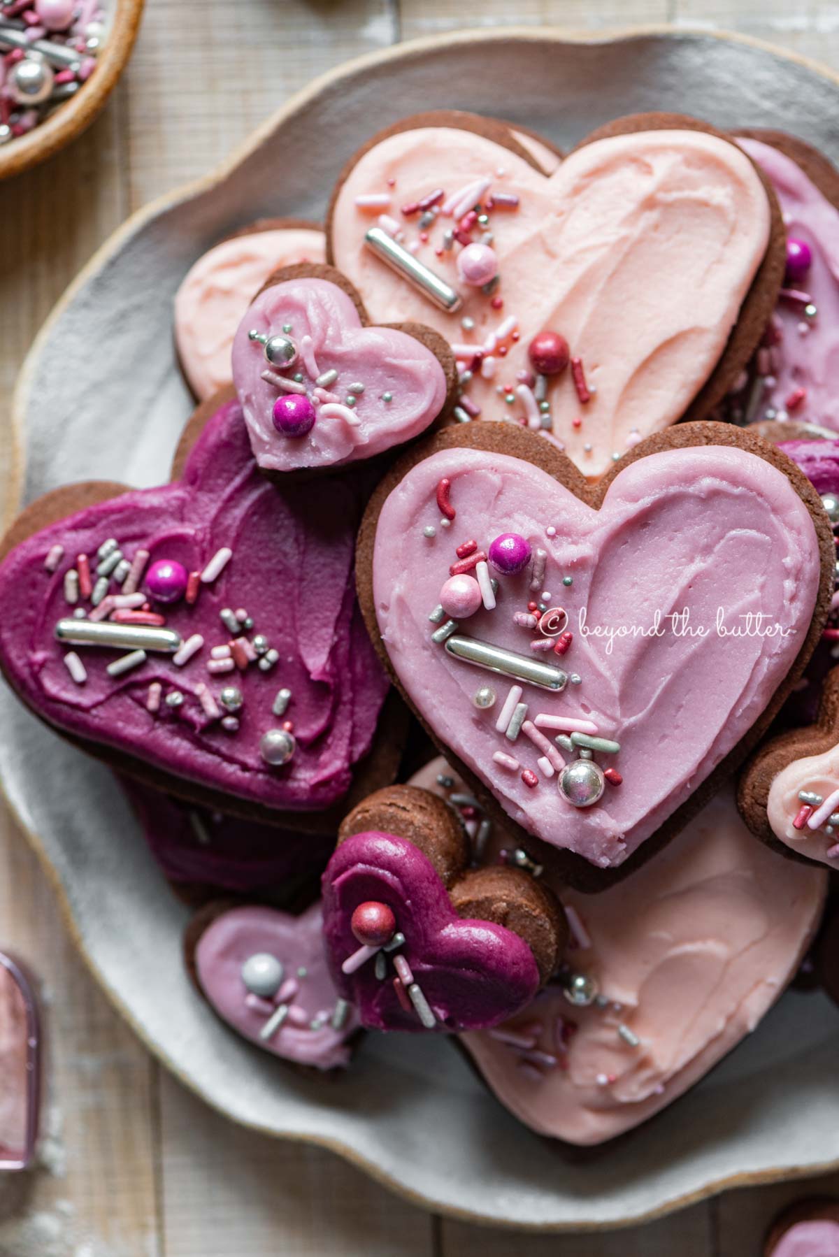 Plate full of heart-shaped chocolate cut out sugar cookies decorated with buttercream frosting and sprinkles.