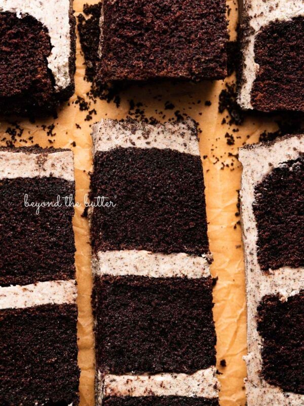 Slices of three layer chocolate cake with oreo buttercream frosting on natural parchment paper.