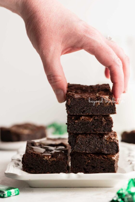 Stacking mint chocolate brownies on a white dessert plate | © Beyond the Butter®
