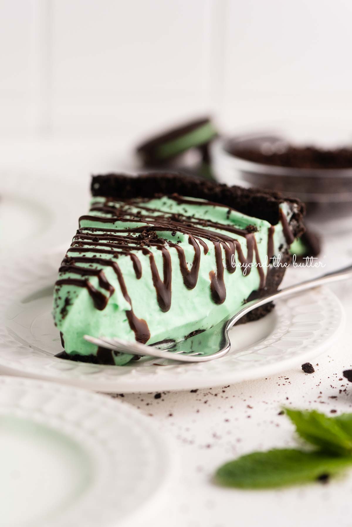 Dessert plates with slices of no bake mint chocolate pie with chocolate syrup drizzled over the top | © Beyond the Butter®