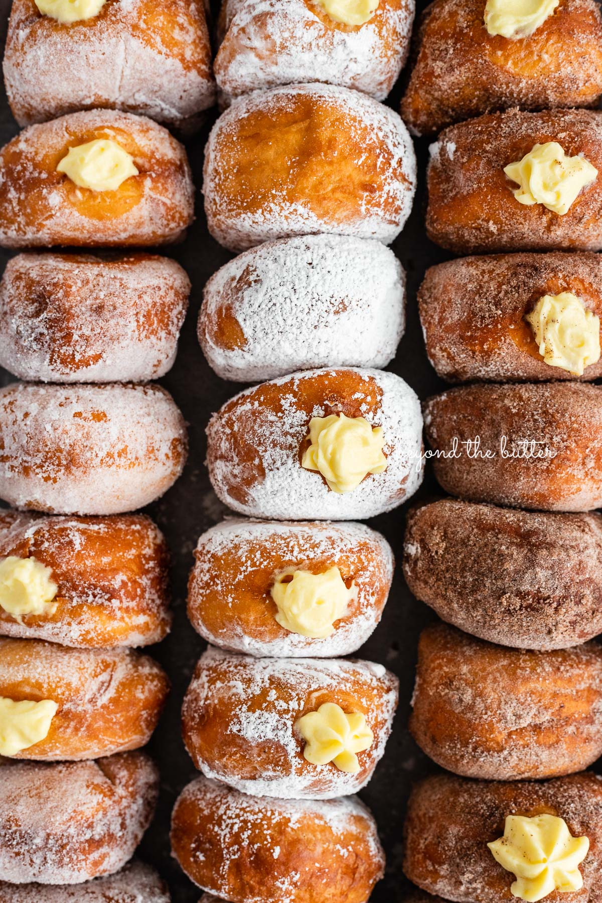 Rows of pennsylvania dutch fasnacht doughnuts filled with pastry cream.