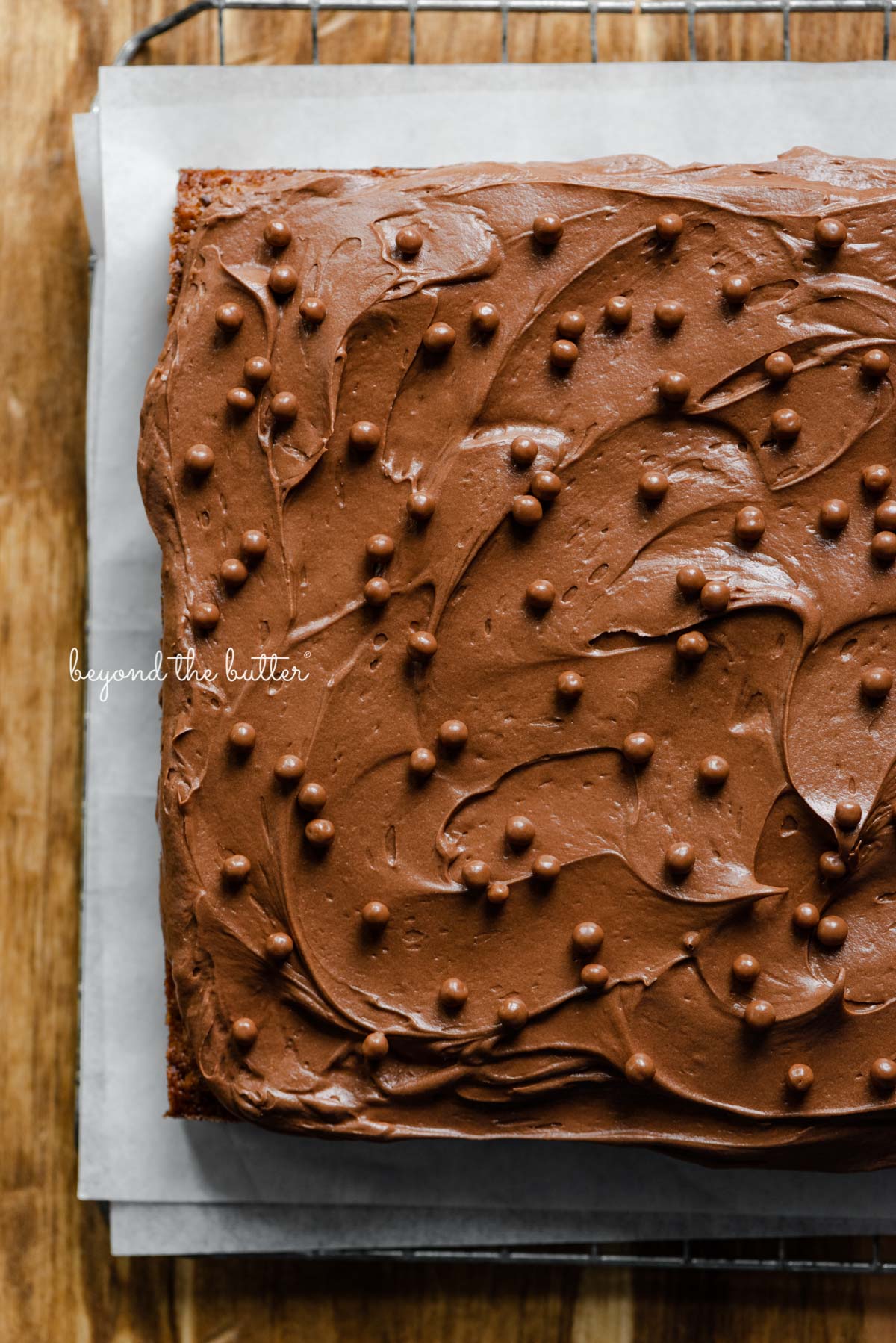 Banana chocolate chip snack cake with chocolate cream cheese frosting on parchment paper and wire cooling rack | All images © Beyond the Butter®