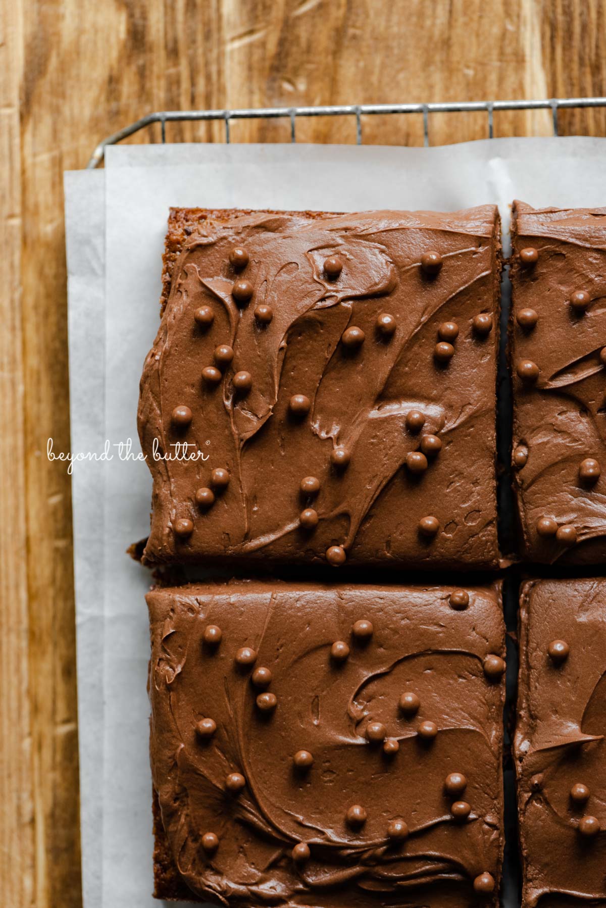 4 square slices of banana chocolate chip snack cake with chocolate cream cheese frosting on parchment paper and wire cooling rack | All images © Beyond the Butter®