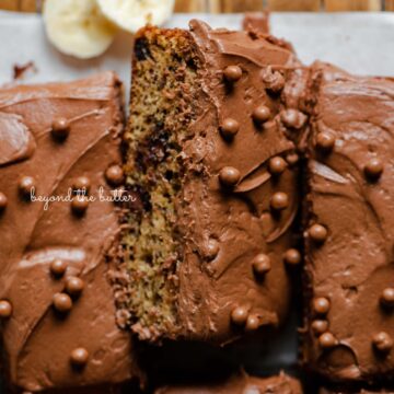 Slices of banana chocolate chip snack cake with chocolate cream cheese frosting on parchment paper lined cooling rack with banana slices | All images © Beyond the Butter®