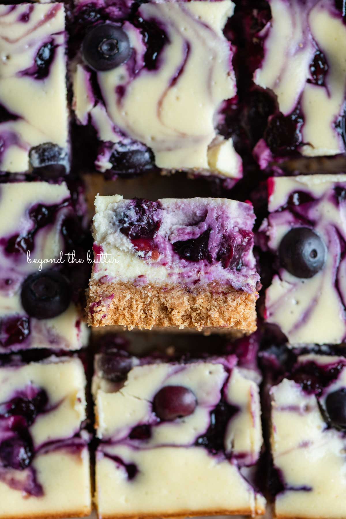 Sliced blueberry swirl cheesecake bars with center bar on its side | © Beyond the Butter®