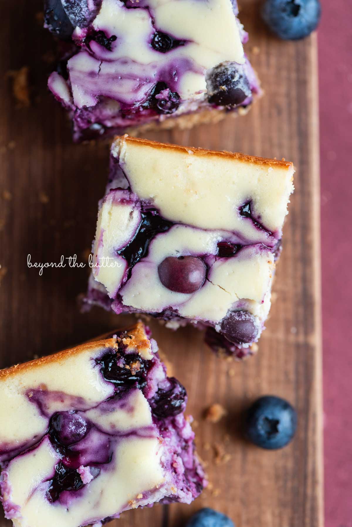 Sliced blueberry swirl cheesecake bars on a vintage cutting board from BeyondtheButter.com | © Beyond the Butter®