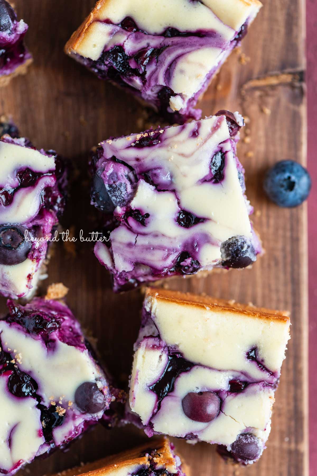 Sliced blueberry swirl cheesecake bars on a vintage cutting board from BeyondtheButter.com | © Beyond the Butter®