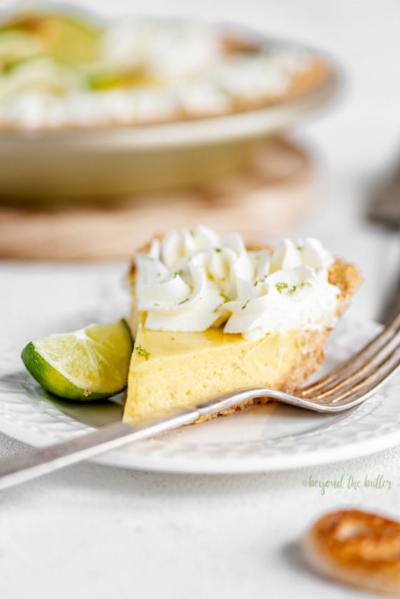 Easy Key Lime Pie decorated with homemade whipped cream, puff pastry twists, and sliced limes | Image and Copyright Policy: © Beyond the Butter, LLC