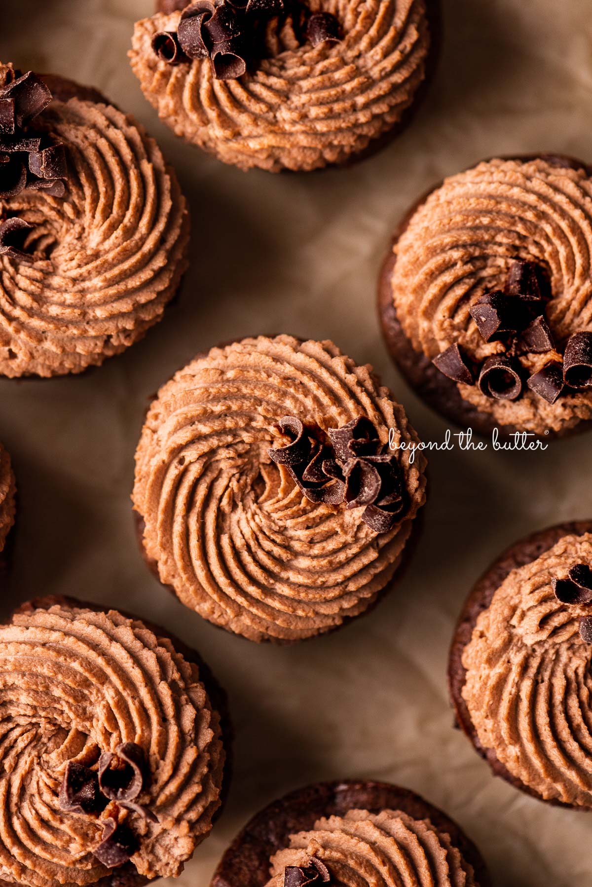 Chewy brownie bites topped with dark chocolate curls on natural parchment paper | © Beyond the Butter®