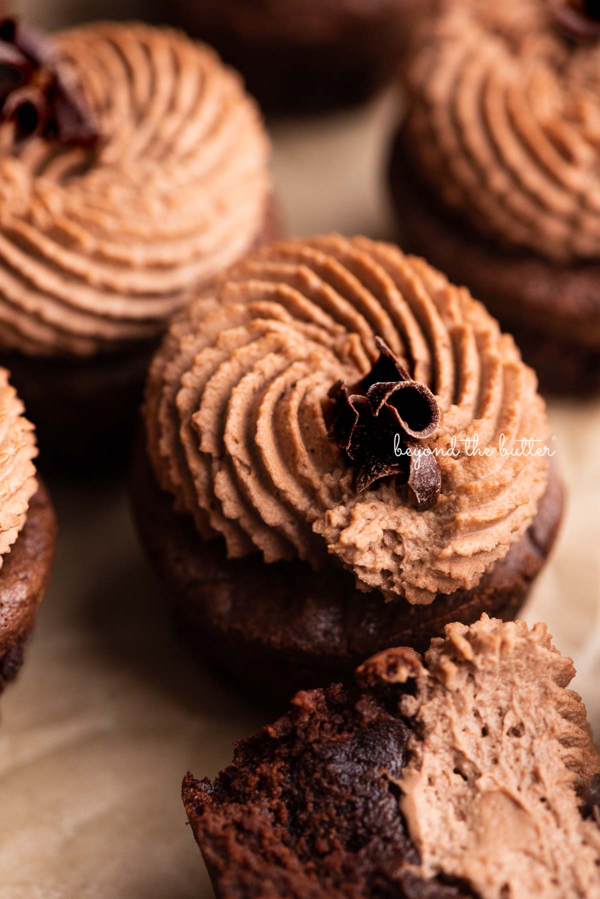 Chewy brownie bites on natural parchment paper with one half eaten brownie bite in the center | © Beyond the Butter®