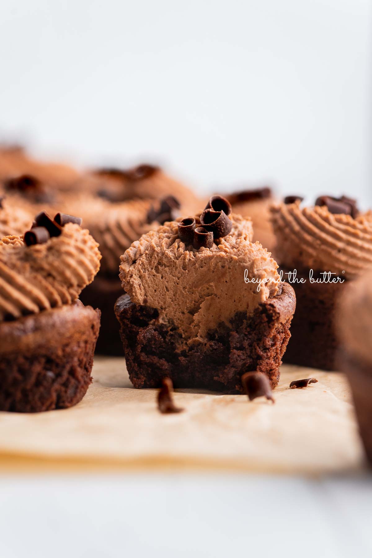 Mini brownie bites on natural parchment paper with one half eaten brownie bite in the center | © Beyond the Butter®