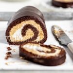 Slices of chocolate pumpkin cake roll with knife on parchment paper lined jelly roll pan.