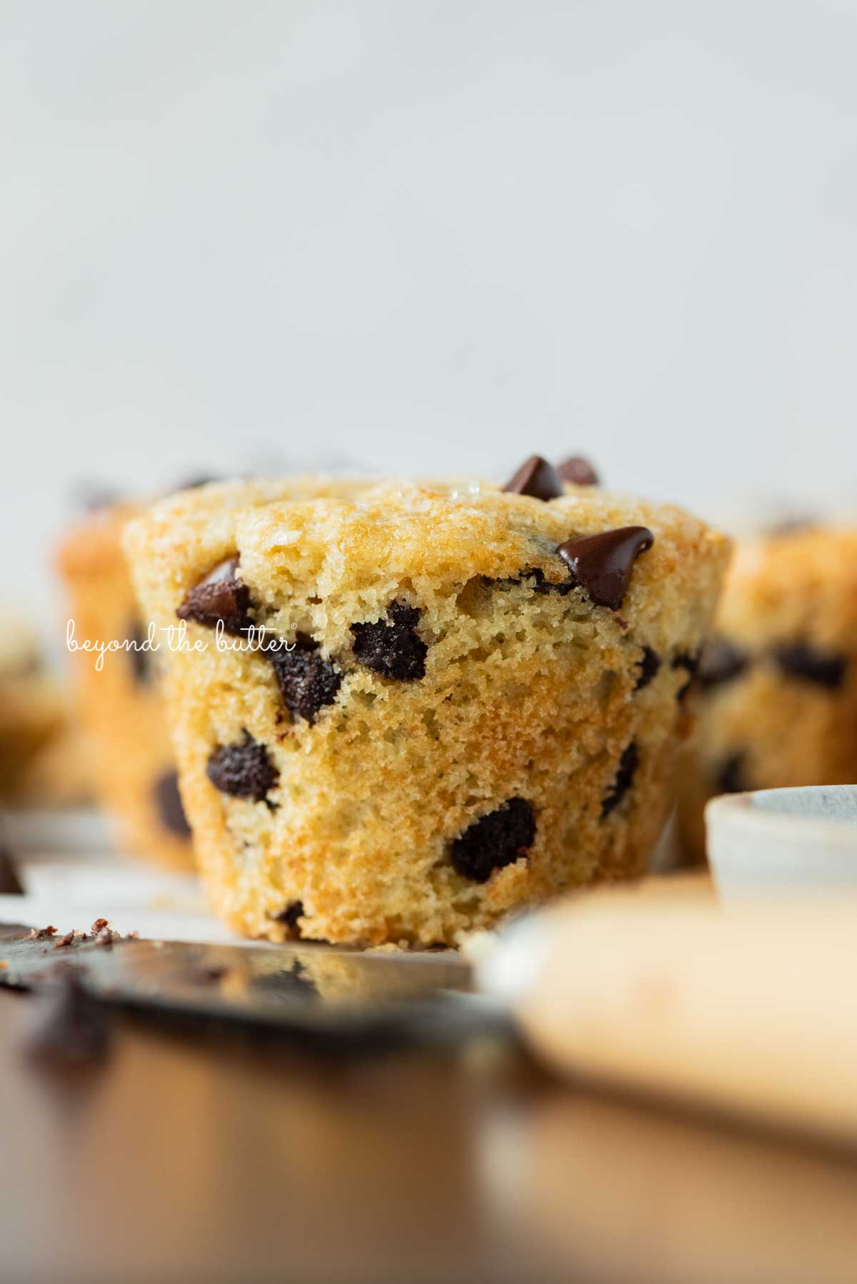 Single unwrapped bakery style chocolate chip muffin on a flattened muffin liner with white background | © Beyond the Butter®