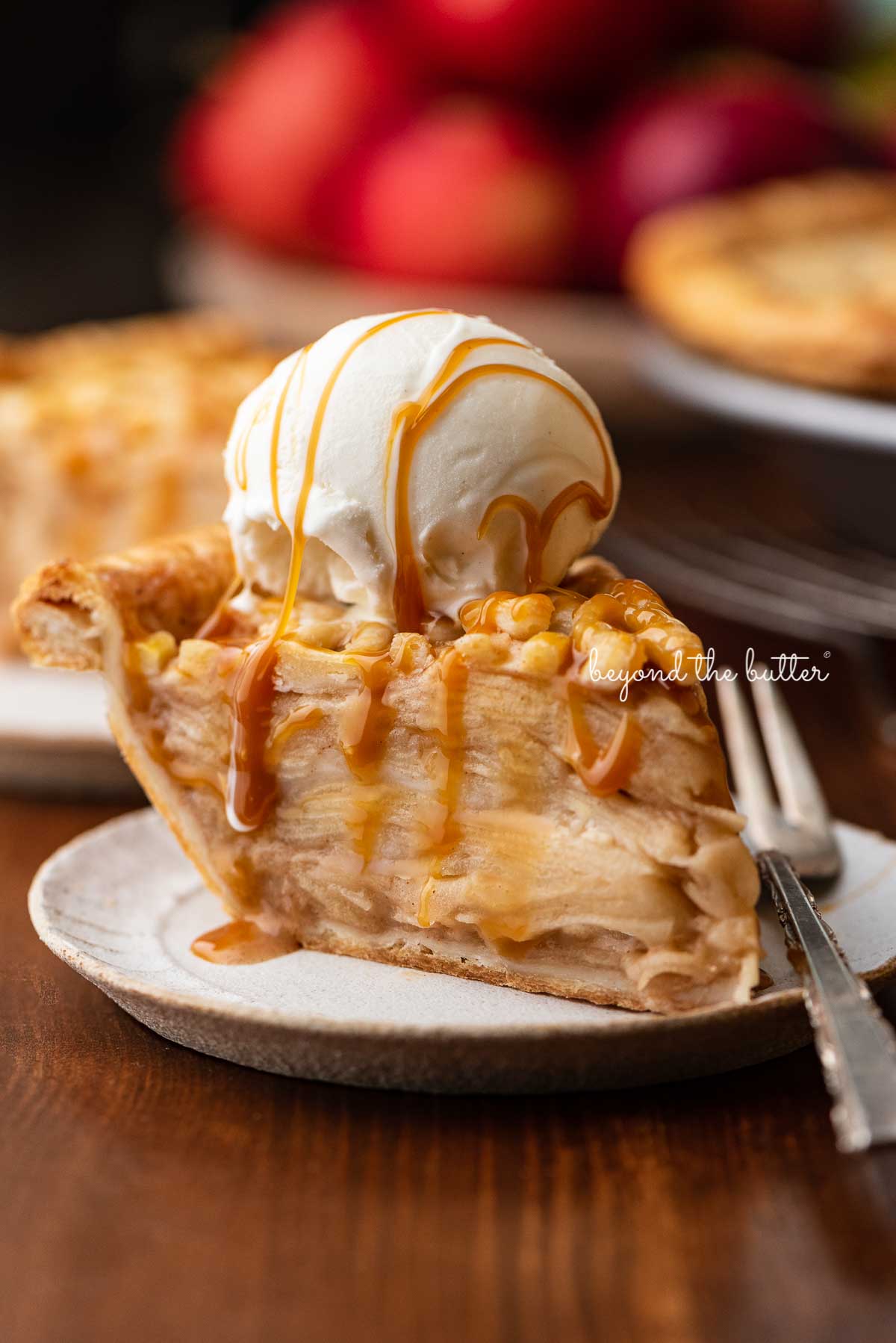 Slice of easy homemade apple pie drizzled with caramel and topped with a scoop of vanilla bean ice cream | © Beyond the Butter®